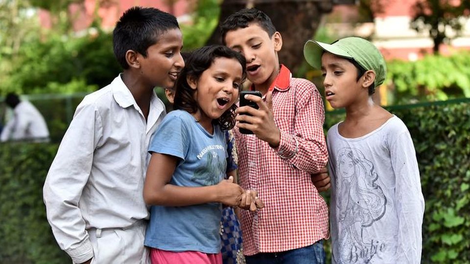 Children gathered around a mobile phone together outdoors.